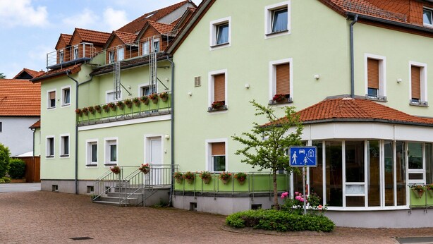Ein mehrgeschossiges Gebäude mit grüner Fassade, einem überdachten Eingang und einem Schild, das eine öffentliche Toilette kennzeichnet.