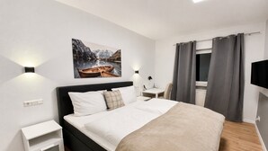 Ein modernes Hotelzimmer mit einem großen Bett, Nachttischen, einem Wand-Fernseher und einem Gemälde einer Berglandschaft.