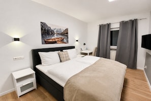 A modern hotel room with a large bed, bedside tables, a mounted TV, and a painting of a mountainous landscape. - Landhotel Rauber Sankt Wendel Double Room (Oberthal)