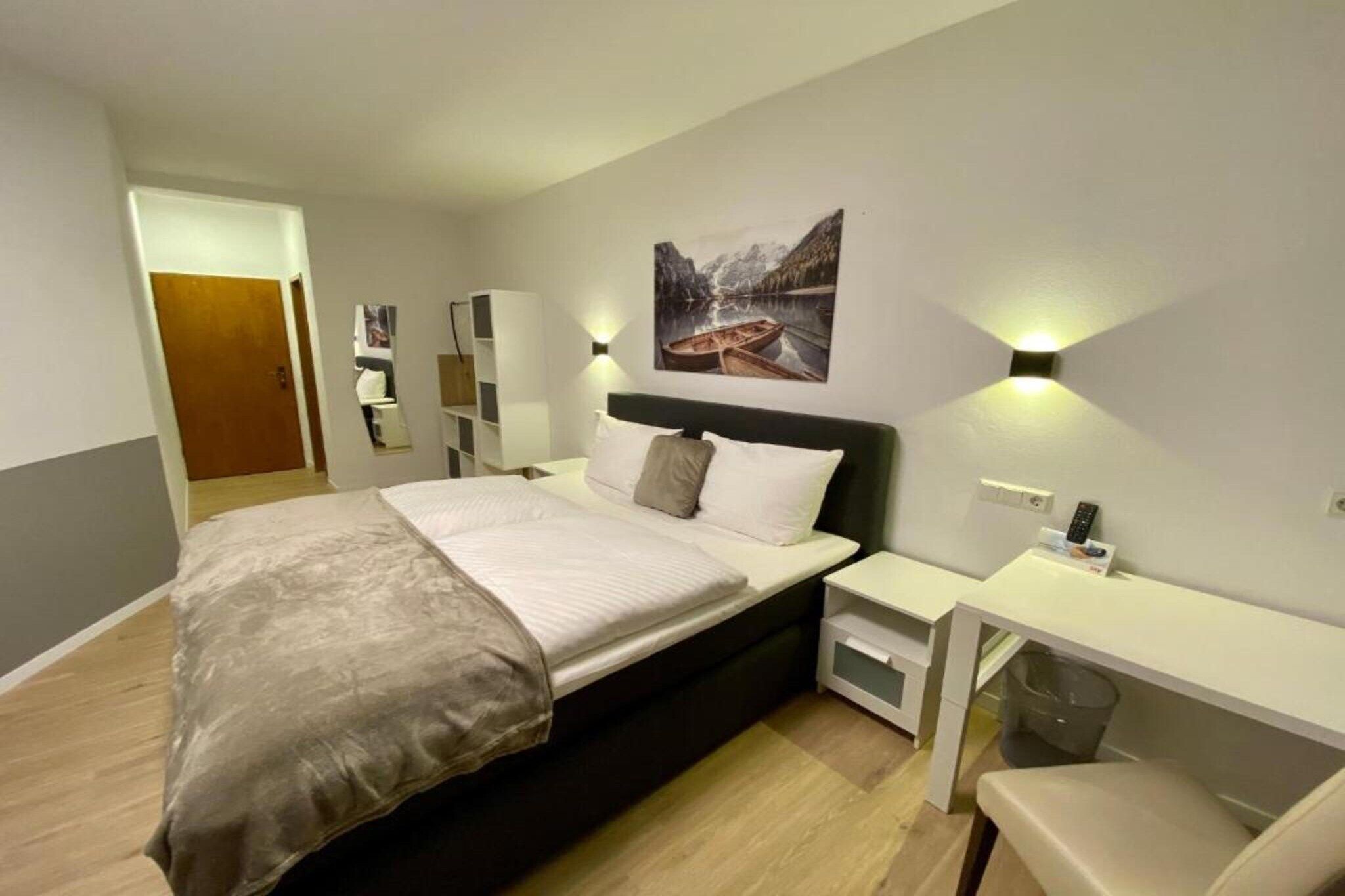 Ein modernes Hotelzimmer mit einem großen Bett, Nachttischen, einem Schreibtisch und einem Bild an der Wand.