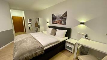 A modern hotel room with a large bed, bedside tables, a desk, and a painting on the wall.