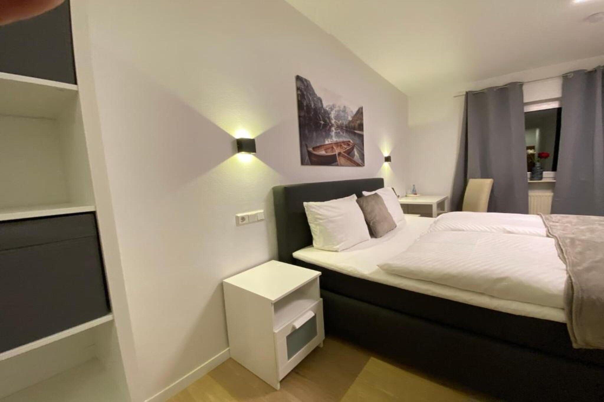 Una habitación de hotel con cama, mesitas de noche, una lámpara de pared y un cuadro.