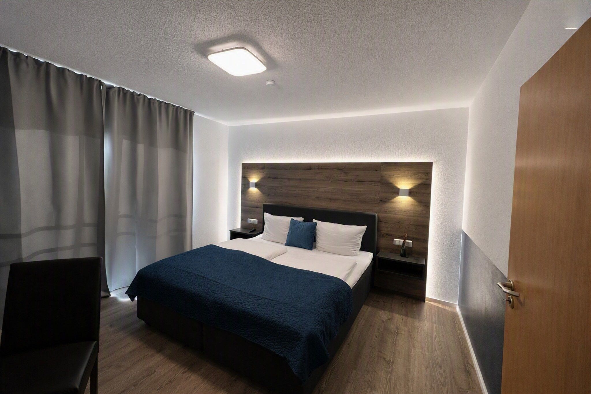 Ein Hotelzimmer mit einem Bett, einem Nachttisch, einem Sessel und einer Tür.