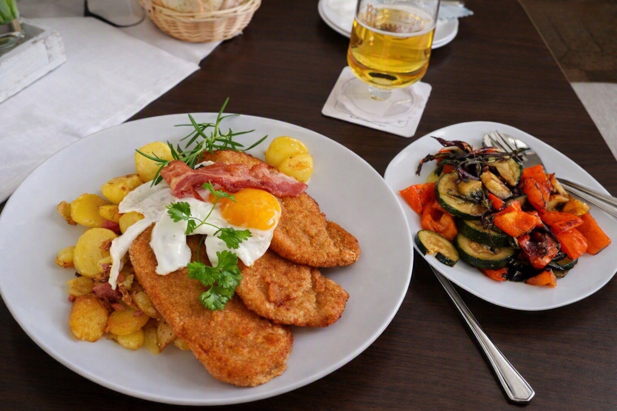 Two plates of food on a table with a glass of beer and a fork.