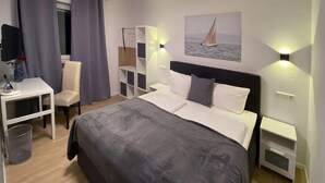Ein Hotelzimmer mit Bett, Schreibtisch, Stuhl, Kleiderschrank und einem Bild an der Wand.