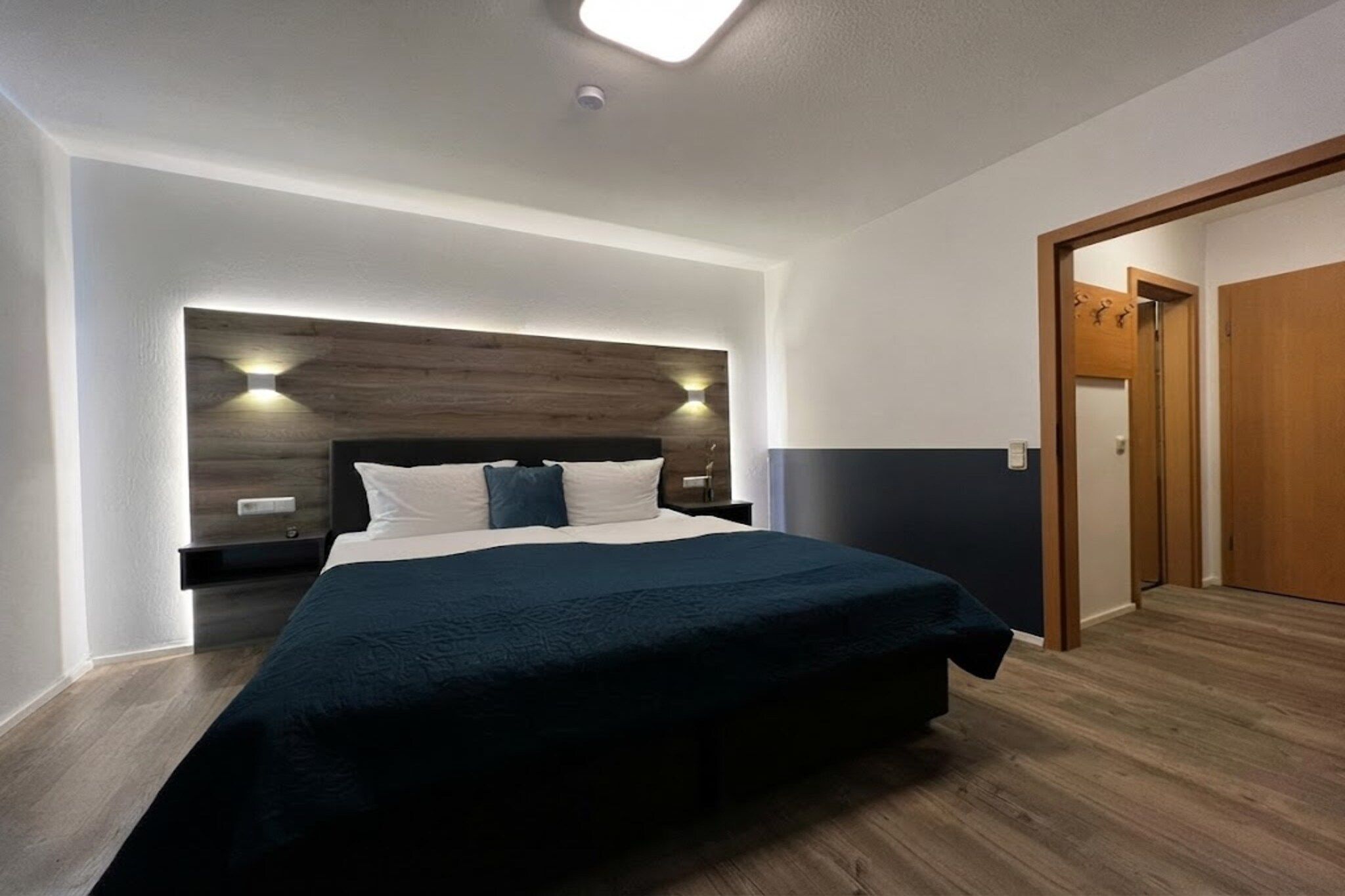A modern bedroom with a large bed, a wooden headboard, and a nightstand.