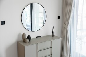 A modern bathroom with a round mirror, a light-colored vanity, and a window with curtains. - StayShort - Chic 1 Bedroom Unit in Dubai Marina that Sleeps 4! (Dubai)