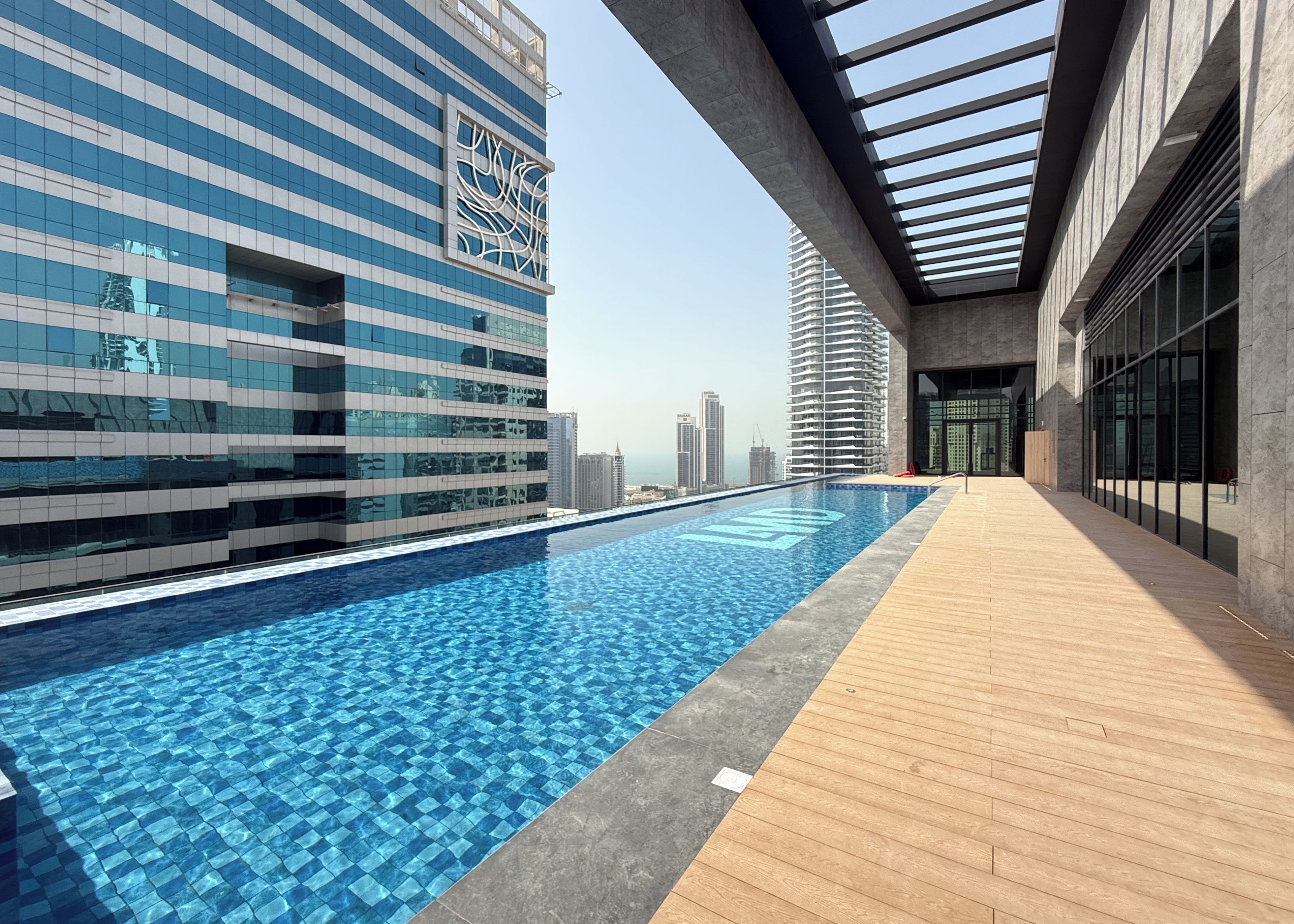 A rooftop pool with a cityscape view, modern architecture, and a wooden deck.
