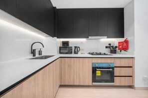 Uma cozinha moderna com armários pretos, bancada branca, micro-ondas Bosch, fogão a gás e máquina de lavar louça.