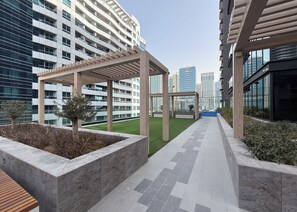 Ein moderner Außenbereich mit einer Holz-Pergola, einer Rasenfläche und einem Weg, der zu einem mehrstöckigen Gebäude mit Balkonen führt.