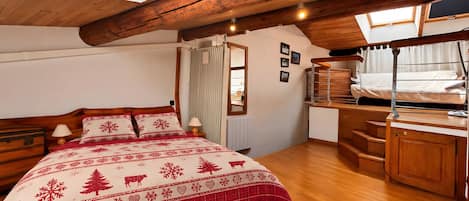 A cozy bedroom with a wooden ceiling, a bed with a red and white patterned bedspread, a desk, and a window with curtains.