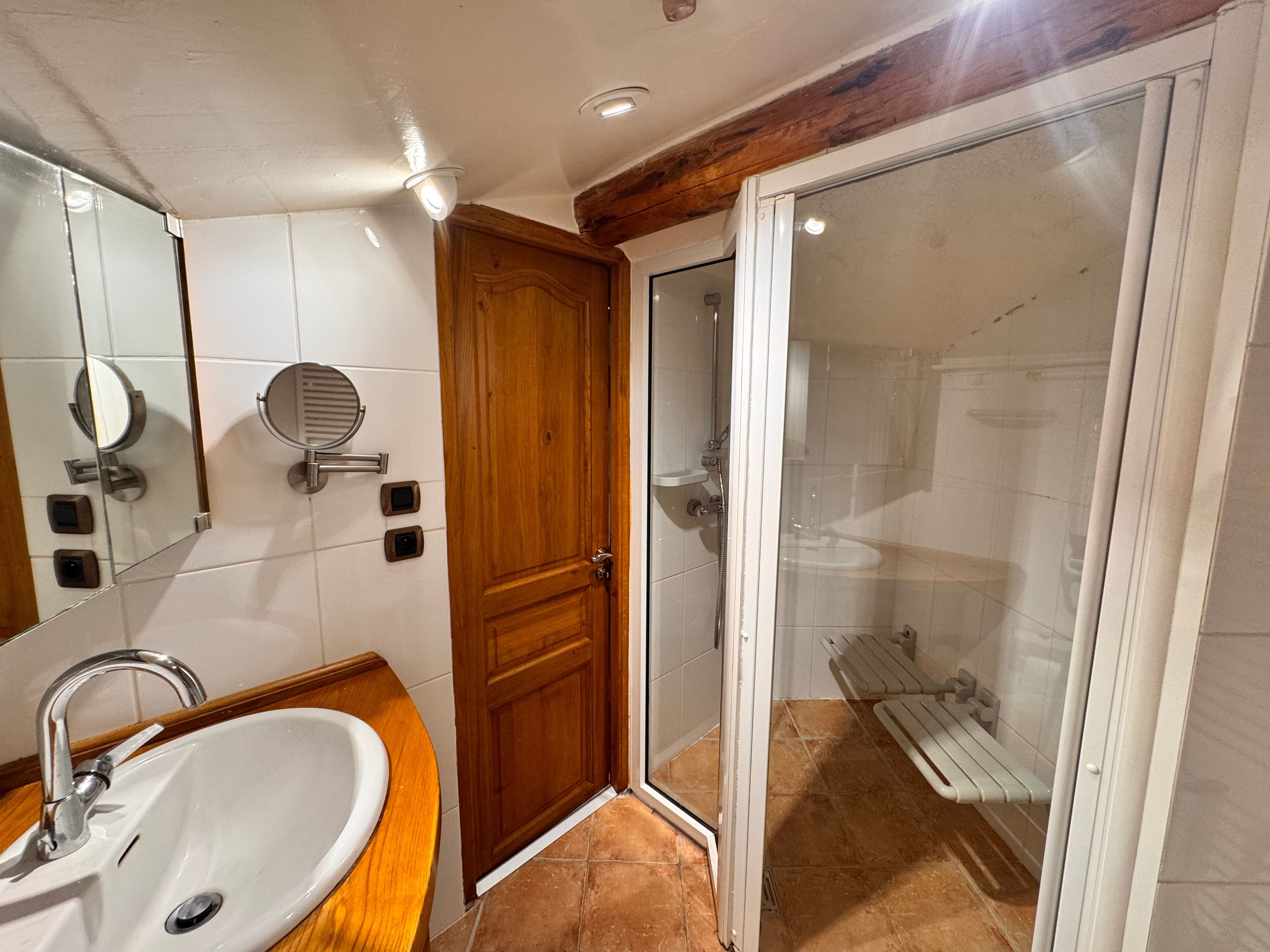 A bathroom with a sink, mirror, wooden door, and a shower area.