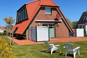 Une maison avec un toit en pente, une antenne parabolique et une terrasse clôturée avec deux chaises.