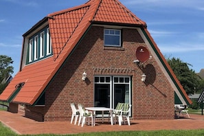 Ein Ziegelhaus mit rotem Ziegeldach, einem großen Fenster und einer Terrasse mit Tisch und Stühlen.