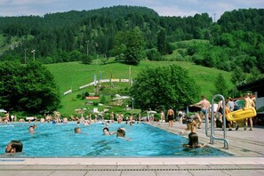 Ein Schwimmbecken mit darin badenden Personen, umgeben von einer hügeligen Landschaft.