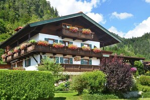 Un chalet traditionnel doté d’un balcon en bois, de nombreuses fenêtres et d’un jardin bien entretenu.