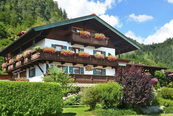 Ein traditionelles Chalet mit Holzbalkon, zahlreichen Fenstern und einem gepflegten Garten.