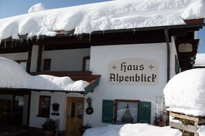 Ein traditionelles Gebäude mit einem Schild, auf dem 'Haus Alpenblick' steht, und verschneiter Umgebung.