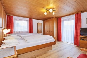 Ein Hotelzimmer mit Holzboden, einem Bett mit weißen Leinen, einem Fernseher und roten Vorhängen.