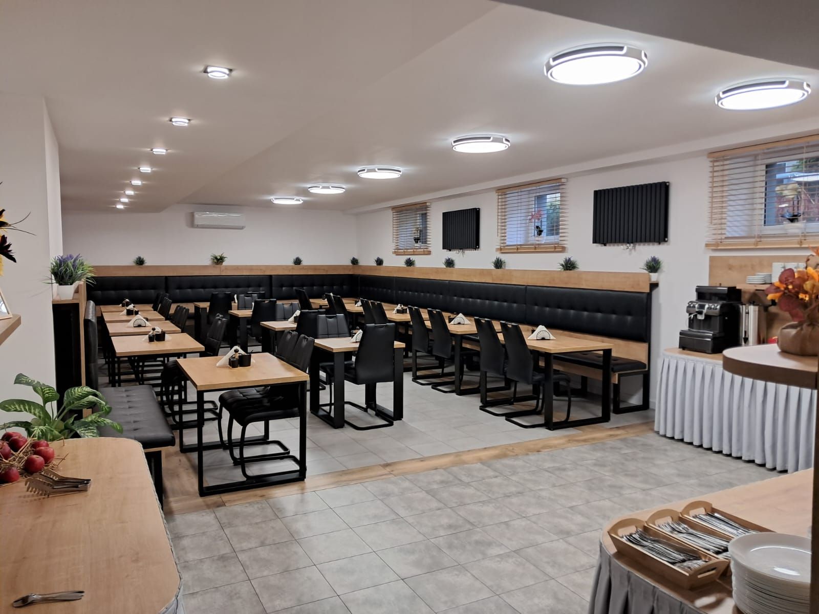 Un espace repas moderne doté de plusieurs tables et de banquettes, d’un éclairage au plafond et d’une machine à café.