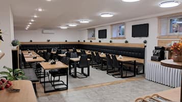 Un espace repas moderne doté de plusieurs tables et de banquettes, d’un éclairage au plafond et d’une machine à café.