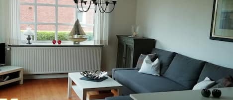 A living room with a sofa, a coffee table, a TV, and a window with a view of a brick building.