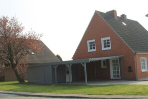 Ein zweigeschossiges Backsteinhhaus mit überdachter Garage und einem Baum im Vordergrund.