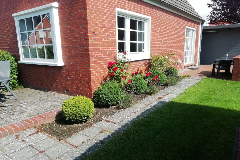 A brick house with two windows, a garage, and a small garden with red flowers and shrubs.