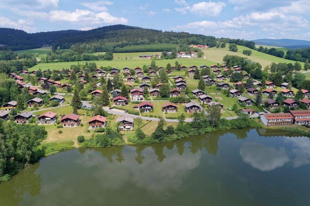 Un pueblo a orillas del lago con casas de techo rojo, cielo despejado y abundante vegetación.