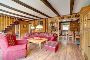 Ein Blockhaushaus-Interieur mit einer Holztreppe, einer rot-weiß gestreiften Couch-Garnitur, einem Holzesstisch und einem Kronleuchter.