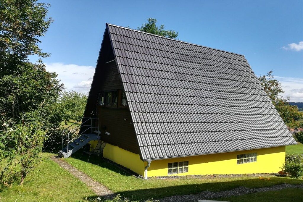 A yellow building with a steeply pitched roof and a staircase leading to a door.