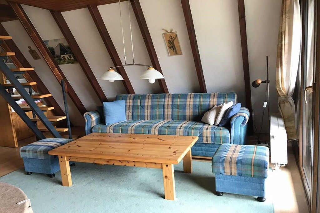 A living room with a sofa, ottoman, and a wooden coffee table. There is a staircase with a railing and a picture on the wall.