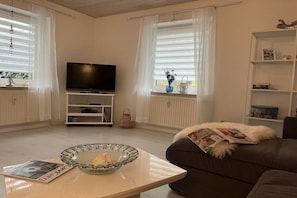 A living room with a television, a glass bowl on a table, and a sofa with a magazine. - Holiday apartment with 1 bedroom (Wurster Nordseeküste)