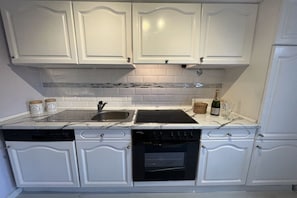 A kitchen with white cabinetry, a dishwasher, an oven, a stovetop, and a sink. - Holiday apartment with 1 bedroom (Wurster Nordseeküste)
