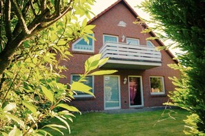 A two-story brick house with a balcony, surrounded by greenery. - Holiday apartment with 1 bedroom (Wurster Nordseeküste)