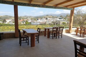 Eine Terrasse im Freien mit Holztischen und -stühlen, einem Fliesenboden und Blick auf ein Dorf und Hügel in der Ferne.