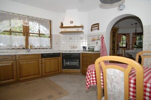 A kitchen with wooden cabinets, a built-in oven, and a window with lace curtains. - Haus Winterberg || Erfweiler (Erfweiler)