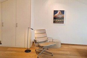 Una silla de oficina moderna con estructura metálica y asiento de cuero, sobre un piso de madera y con un cartel de una montaña en la pared.