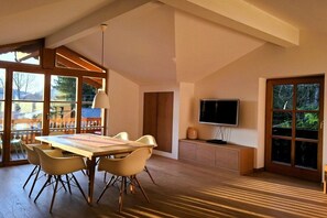 A spacious room with a large dining table, comfortable chairs, a television, and large windows offering a view of the outdoors. - Floor cutting suites "Luxburg" (Tegernsee)