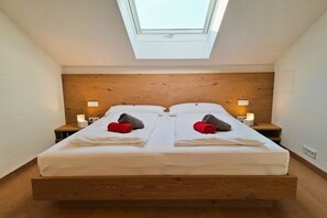 A twin bed with a wooden headboard, two bedside tables with lamps, and a skylight above. - Floor cutting suites "Luxburg" (Tegernsee)
