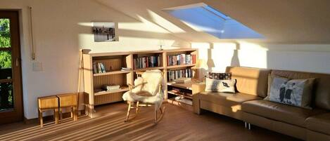A cozy living room with a wooden floor, a rocking chair, a sofa, a bookshelf, and a skylight.