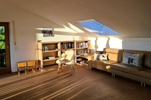 A cozy living room with a wooden floor, a rocking chair, a sofa, a bookshelf, and a skylight. - Floor cutting suites "Luxburg" (Tegernsee)