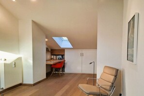 Una habitación con tragaluz, radiador, escritorio con libros, una silla roja y un sofá.