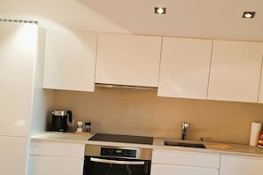 A modern kitchen with white cabinets, a built-in oven, a coffee maker, and a sink. - Floor cutting suites "Luxburg" (Tegernsee)