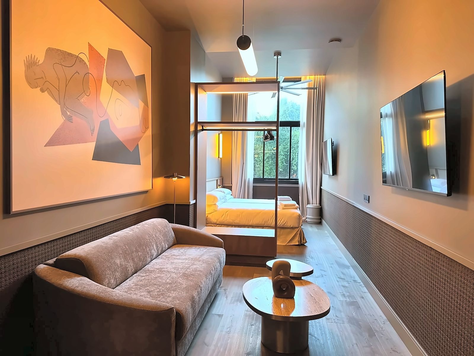 Een hotelkamer met een bank, een ronde tafel, een bed met gordijnen, een televisie en een schilderij aan de muur.