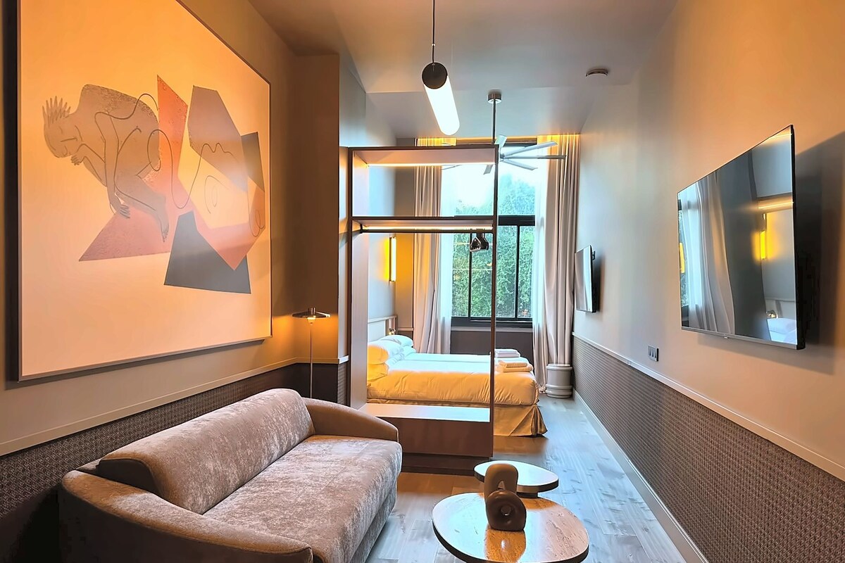 Een hotelkamer met een bank, een ronde tafel, een bed met gordijnen, een televisie en een schilderij aan de muur.