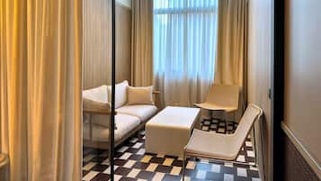 Een moderne hotelkamer met een bank, een klein tafeltje, een rieten stoel en een geruit vloerkleed.