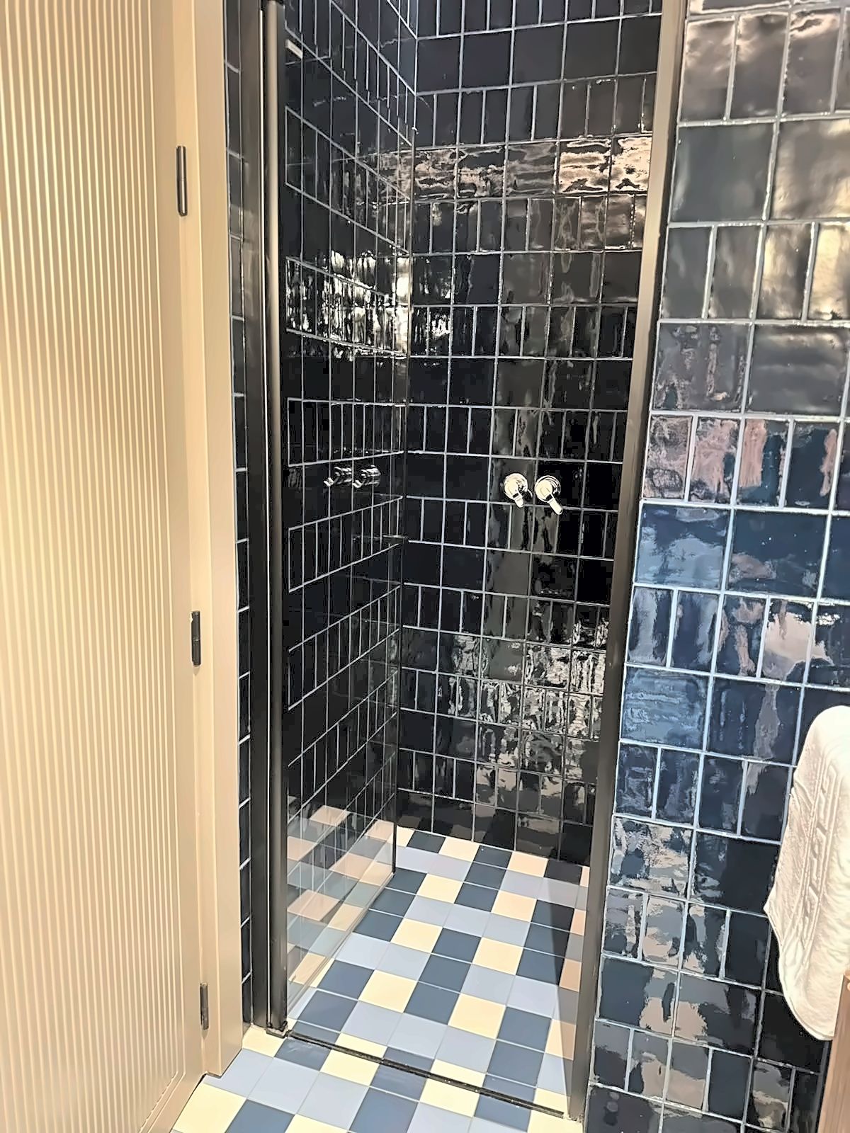 Un baño con piso a cuadros, cabina de ducha de vidrio y pared de azulejos.