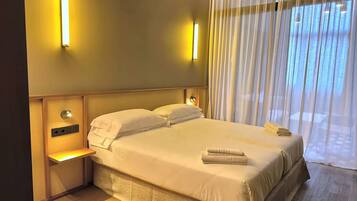 A hotel room with a bed, bedside lamps, a nightstand, and a window with curtains.