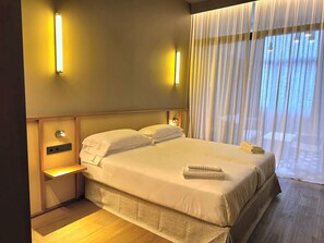 A hotel room with a bed, bedside lamps, a nightstand, and a window with curtains. - La Ría Urban Apartments (Bilbao)